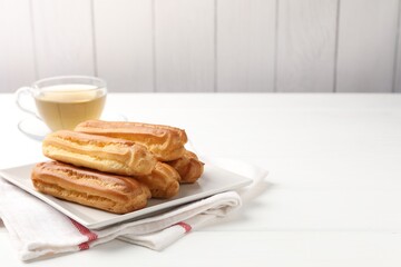 Tasty eclairs and tea on white wooden table. Space for text