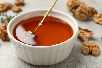 Honey in bowl and walnuts on light grey table, closeup