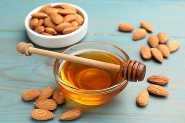 Honey in bowl, almonds and dipper on light blue wooden table, closeup
