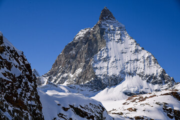 Close view of the Matterhorn covered in winter snow, rising sharply under a deep blue sky. Iconic Swiss alpine landscape with dramatic textures and prisitine mountain scenery.