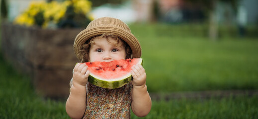 Adorable little girl eating watermelon sitting on the grass in the park