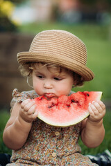 Adorable little girl eating watermelon sitting on the grass in the park