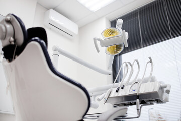 Empty dental chair positioned in modern dental office with overhead examination light and dental instruments arranged on equipment, clinical setting prepared for patient appointment