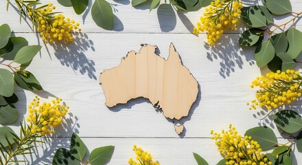 Wooden Australia map framed by golden wattle and green eucalyptus leaves on white wooden background for national identity concept and natural celebration