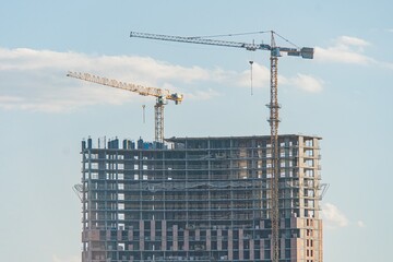 Close-up of a bustling construction site under clear skies, featuring an incomplete high-rise...