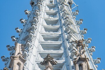 Old Gothic Roman Catholic church tower, intricate carvings, multiple statues, robust design with arches and buttresses, light color contrasting dark sky, daytime natural lighting