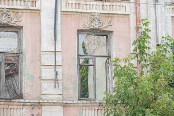 Old European city facade, central large window, intricate design, solid columns, smaller left window, muted color palette gray shades, small plants, ground level perspective, architectural complexi