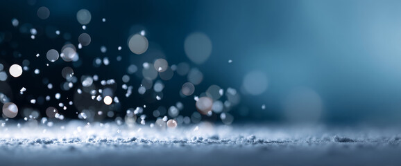 Close-up of snowflakes falling and sparkling on a cold surface with bokeh light effects in a wintery blue background