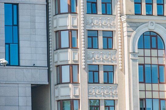 A modern urban building facade, featuring multiple levels, arched and rectangular windows with decorative molding and columns Shuttered windows add a classical touch Earthy color palette beige wal