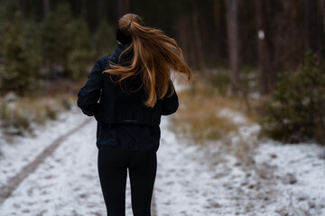 Cold weather training: Woman in thermal running gear runs down a snowy dirt road on an overcast...