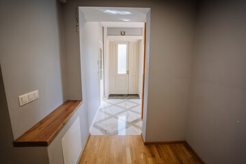 Modern hallway with wooden accents and marble flooring, leading to a bright entrance door, showcasing contemporary interior design and inviting atmosphere