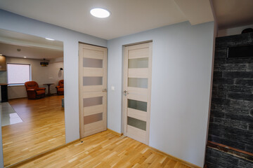 Fototapeta premium Modern interior design featuring two wooden doors with glass panels, light blue walls, and wooden flooring, creating a spacious and inviting atmosphere in a contemporary home