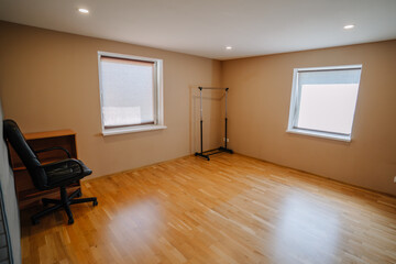 Spacious empty room with wooden flooring, two windows allowing natural light, and minimal furnishings, creating a serene and inviting atmosphere for various uses