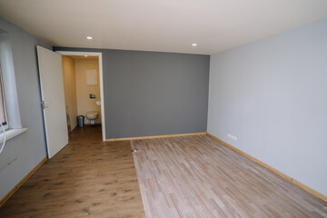 Empty room with wooden flooring and gray walls, featuring an open door leading to a bathroom, showcasing minimalistic interior design and spacious ambiance