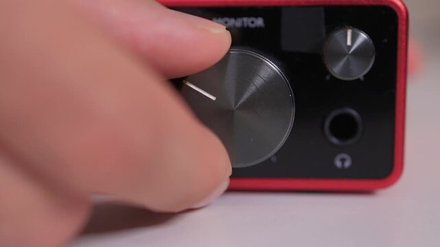 Adjusting external sound card knob, Precise control over audio output through knob rotation, Modifying sound levels using detailed textured dial on external audio interface