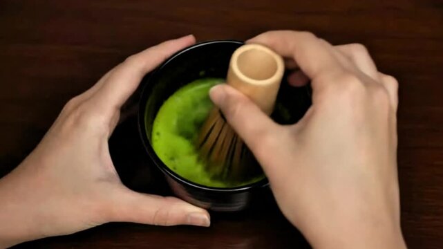 video, closeup, making matcha drink, hands stirring matcha with chasen in a black bowl, Japanese drink