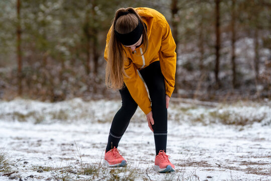 Close-up of a woman outdoors clutching her lower leg and knee in visible discomfort. Image represents shin splints, joint stress, and running injuries, suitable for medical, therapy