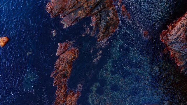 Footage over the wonderful deep blue water splashing by the rocks. Bare brown rocky shore of the sea.