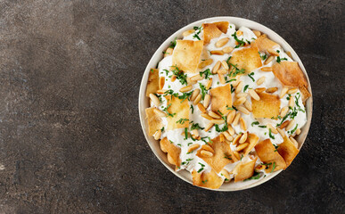 Authentic arabic fatteh with pita bread, yogurt sauce, pine nuts and herbs on gray background. Copy space. Top view.