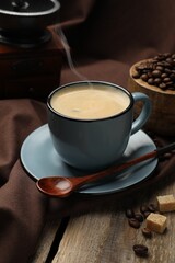 Aromatic coffee in cup, beans, brown sugar and grinder on wooden table, closeup