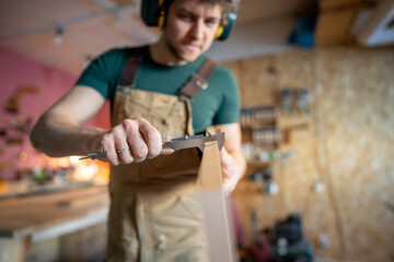 Craftsman using vernier calipers to verify plank thickness during wood processing, selective focus. Closeup hands measuring checking, joinery workshop, carpentry tools, skilled manual work job