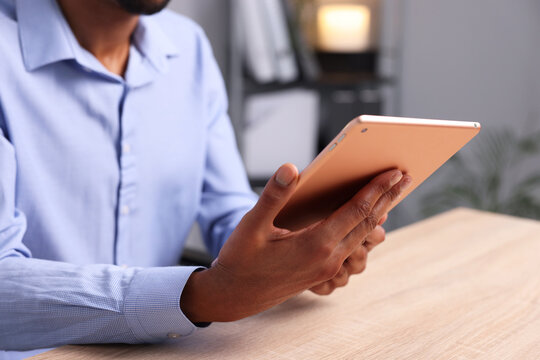 African-american man using tablet at wooden table indoors, closeup - Powered by Adobe
