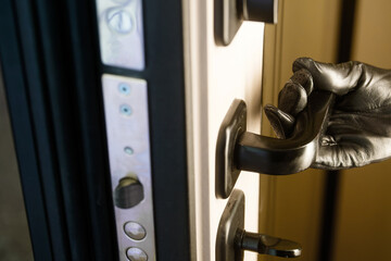 Hand in black leather glove opening armored door handle from inside. Concept of illegal squatter, okupas, burglary, and thief entering house without leaving fingerprints. Photo