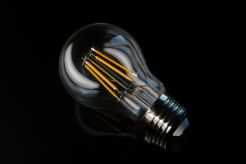 Close up of modern LED filament lamp lying on black glass background with reflection. Electric equipment for energy saving, ecology, and efficiency. Photo
