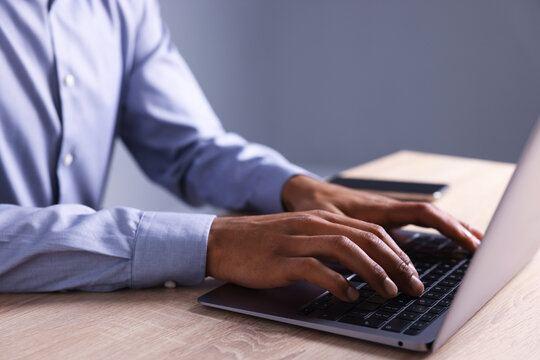 African-american man using laptop at wooden table indoors, closeup