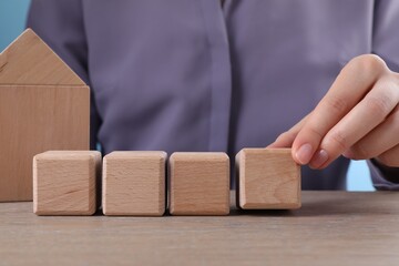 Woman putting cube next to others on wooden table, closeup. Space for design