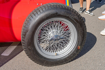 Naklejka premium Close-up view of a vintage Alfa Romeo Formula 1 wheel, black with chrome spokes, in red car background, smooth asphalt, silver hubcap, outdoor setting, vibrant red v - Kyiv, Ukraine - September 21, 20