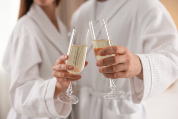 Couple in bathrobes with glasses of sparkling wine indoors, closeup