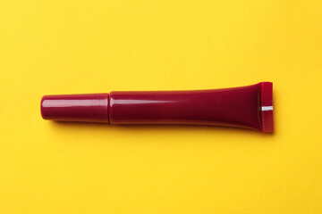 Beautiful dark red lip gloss on yellow background, top view