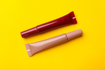 Different lip glosses on yellow background, flat lay