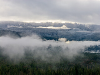 Obraz premium Snowy Mountain Range Above Forest Clouds in BC, Canada — Misty Winter Morning Panorama View