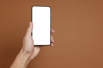 Man holding smartphone with blank screen on brown background, closeup. Mockup for design
