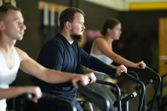 Focused motivated bearded guy leading healthy active lifestyle doing cardio workout on air resistance bike in gym..