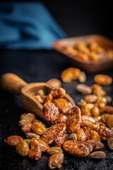 Nuts coated in sugar glaze in scoop on black table.