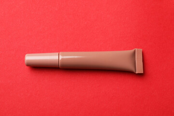 Beautiful nude lip gloss on red background, top view