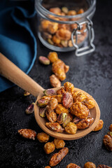 Nuts coated in sugar glaze on wooden spoon on black table.