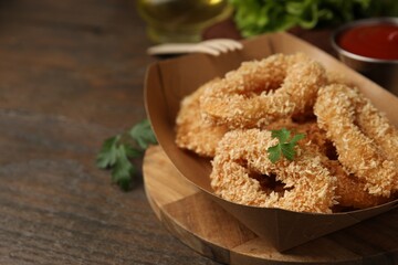 Deep fried squid rings with parsley in takeaway paper box on wooden table, closeup. Space for text