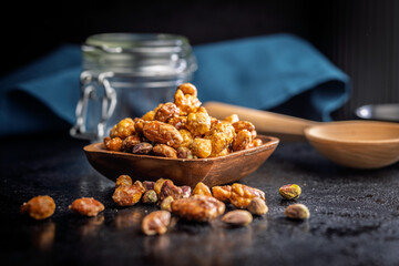 Nuts coated in sugar glaze in bowl on black table.