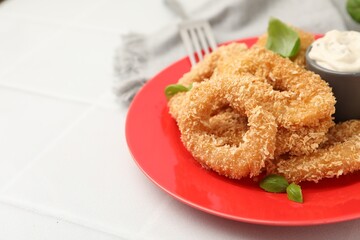 Deep fried squid rings with basil and sauce on white tiled table, closeup. Space for text
