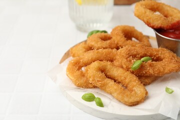 Deep fried squid rings with basil and ketchup on white tiled table, closeup. Space for text