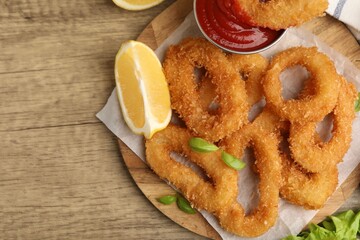 Deep fried squid rings with lemon slice, basil and ketchup on wooden table, top view