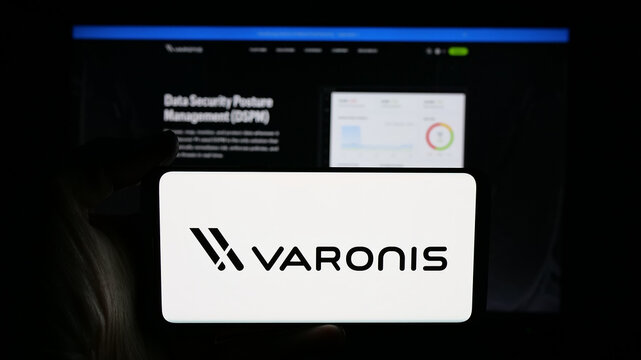 Stuttgart, Germany - 11-21-2025: Person holding cellphone with logo of US software company Varonis Systems Inc. on screen in front of webpage. Focus on phone display.
