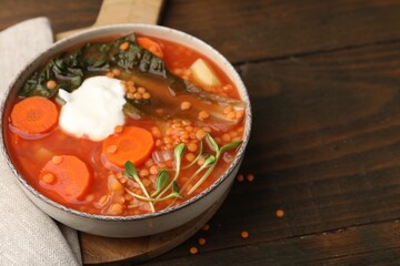Tasty lentil soup with sour cream and vegetables in bowl on wooden table, closeup. Space for text