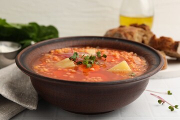 Tasty lentil soup in bowl on white tiled table, closeup