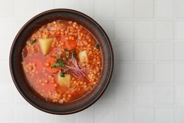 Tasty lentil soup in bowl on white tiled table, top view. Space for text