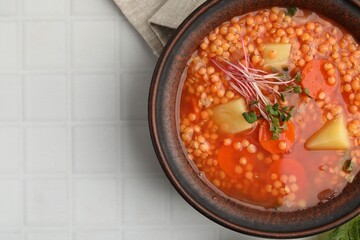Tasty lentil soup in bowl on white tiled table, top view. Space for text